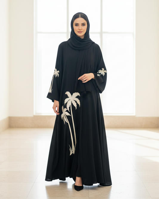 Woman wearing a black abaya with white palm tree patterns in a bright room.