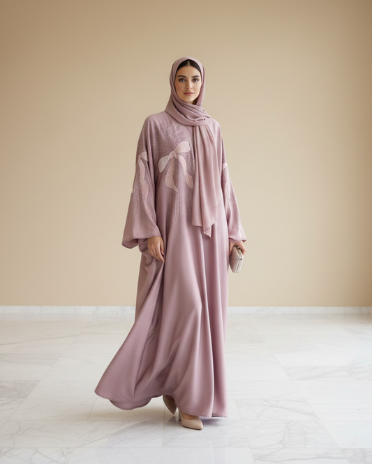 Woman wearing a long, light pink dress and hijab standing in a minimalistic room with beige walls and white floor.