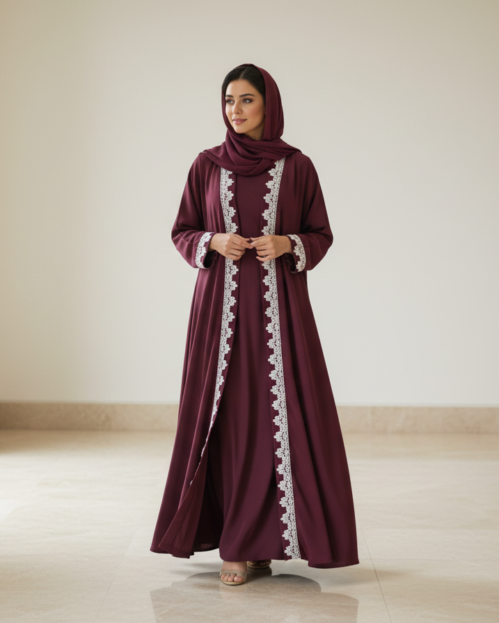 Woman wearing a burgundy abaya with white lace details in a minimalistic room.